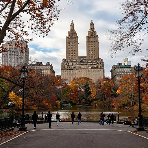 Photograph of New York City's Pennsylvania Station with twin towers, framed by autumn foliage, people walking on a park pathway, and street lamps. Over