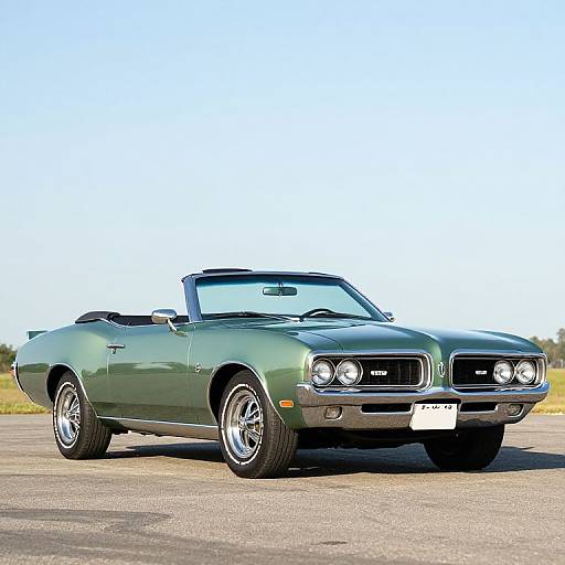 Photograph of a classic green 1970s Ford Mustang convertible with a white license plate, parked on a sunny, open asphalt surface.