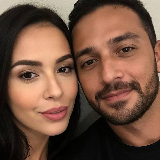 Photograph of a smiling couple with fair skin; woman has long black hair, brown eyes, and pink lipstick, man has short black hair, beard