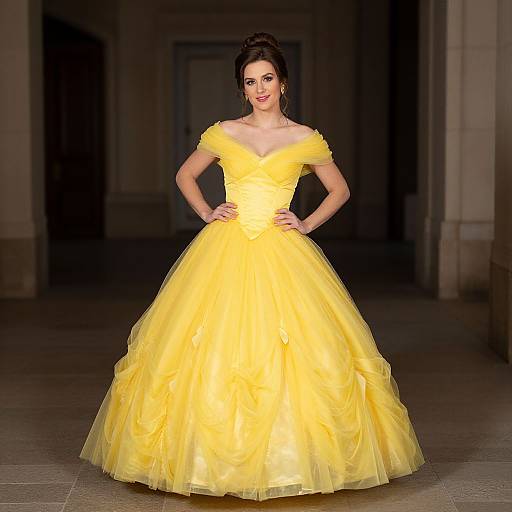Photograph of a woman with dark hair in an off-shoulder, bright yellow ball gown, standing confidently in a dimly lit hallway.
