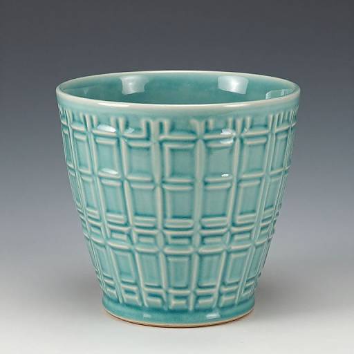 Photograph of a turquoise ceramic cup with a grid-like, raised pattern, against a gradient blue to white background.