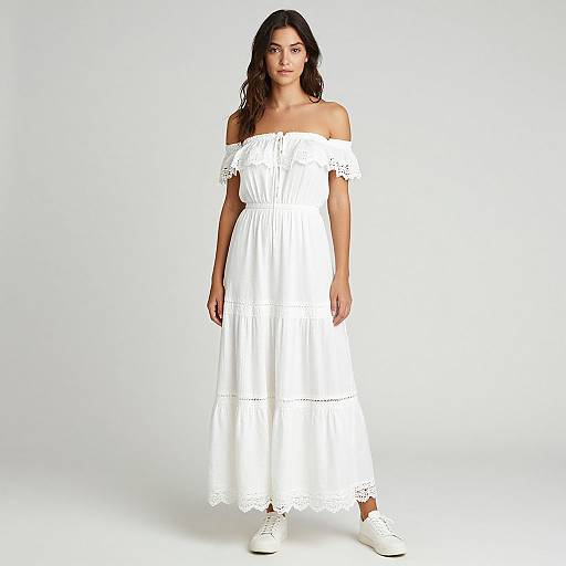 Photograph of a young woman with long, wavy brown hair, wearing an off-shoulder, white lace dress and white sneakers, standing against