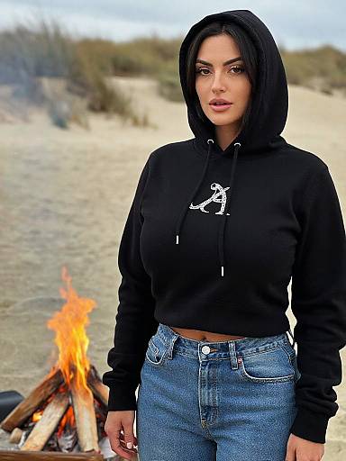 Photograph of a woman with olive skin, dark hair, and full lips, wearing a black hoodie and blue jeans, standing in a sandy, desert