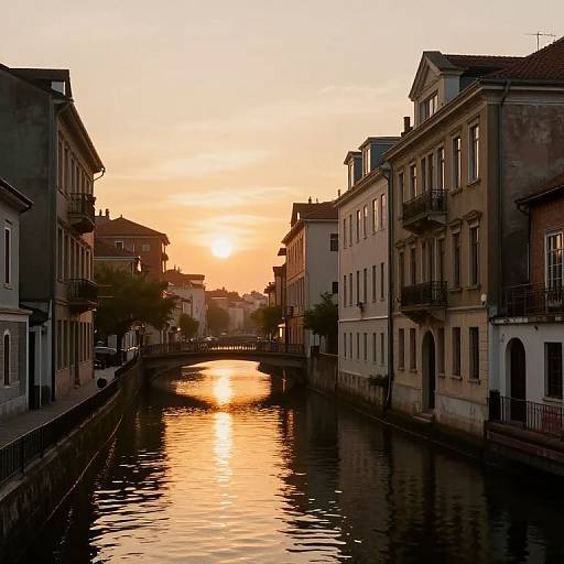 Photograph of a serene canal at sunset, with warm orange and yellow hues reflecting off the water, surrounded by narrow European-style buildings.