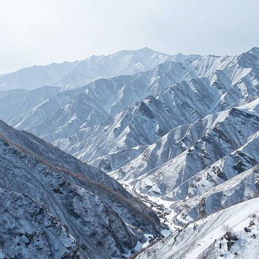 Photograph of snow-covered, rugged mountain range with sharp peaks and steep slopes under a clear, bright blue sky.