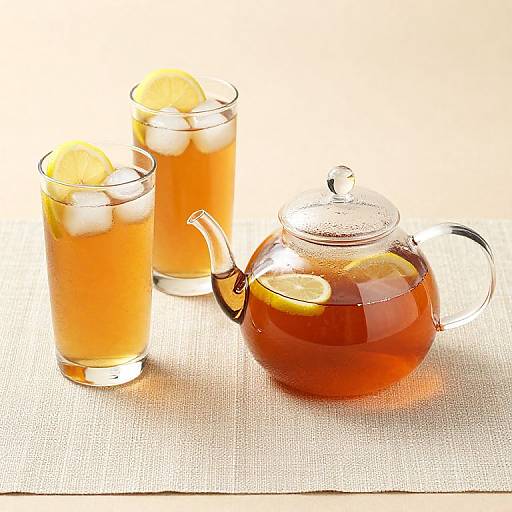 Photograph of two glass cups with lemon slices in orange tea, and a glass teapot with lemon slices, on a white textured cloth.