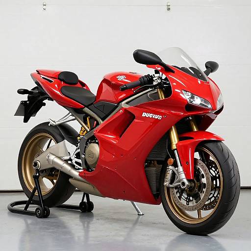 Photograph of a vibrant red Ducati sport motorcycle with gold wheels, black seat, and sleek design, standing on a black kickstand.