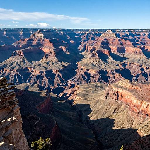 Photograph of Grand Canyon at sunset; showcasing rugged, multicolored rock formations, deep shadows, and a bright blue sky with scattered clouds.