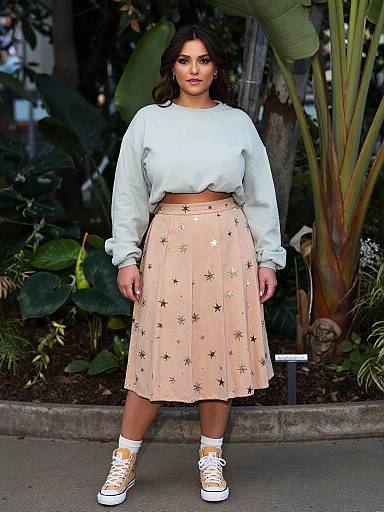 Photograph of a curvy woman with medium brown skin, dark wavy hair, wearing a light blue crop sweater, pink star-patterned skirt,