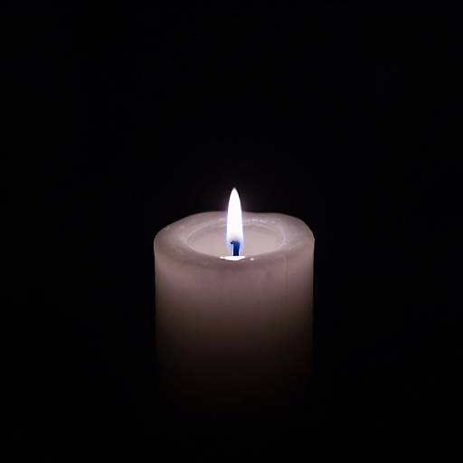Photograph of a glowing white candle with a small blue flame centered against a completely black background.