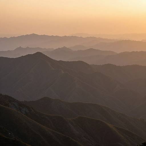 Photograph of a serene mountain range at sunset, with layers of dark, shadowy hills fading into the soft, golden-orange sky.