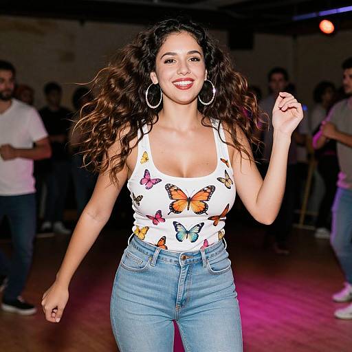 Photograph of a smiling Latina woman with long curly brown hair, wearing a white tank top with colorful butterfly prints, blue jeans, and large hoop earrings
