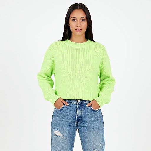 Photograph of a young woman with long black hair, wearing a bright neon green sweater and blue, distressed jeans, standing against a plain white background,