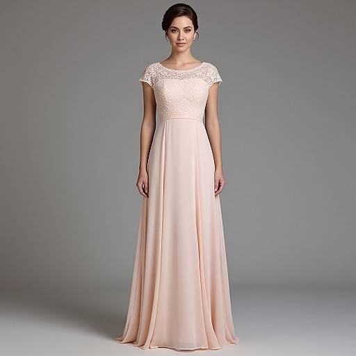 Photograph of a woman with dark hair in an elegant, floor-length, pale pink lace-trimmed gown, standing against a gray gradient background.