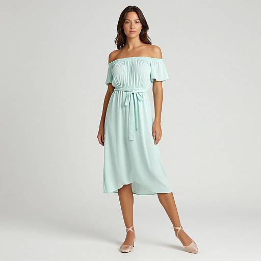 Photograph of a woman with dark hair, wearing an off-shoulder, light blue dress and white sandals, standing against a plain white background.