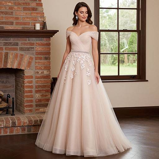 Photograph of a smiling woman in an off-the-shoulder, white lace wedding gown with floral embroidery, standing in front of a brick fireplace and