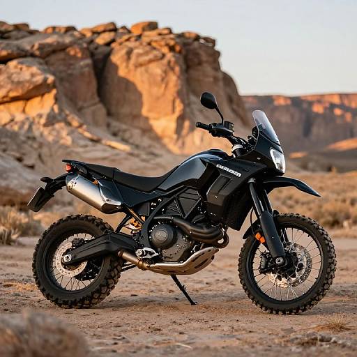 Photograph of a black adventure motorcycle with thick tires, metallic exhaust, and a clear windshield, set against a sunlit desert landscape with rocky cliffs in