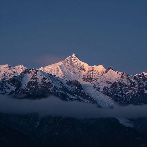 Photograph of a snow-capped mountain peak illuminated by golden light, set against a deep blue sky and shrouded in mist.