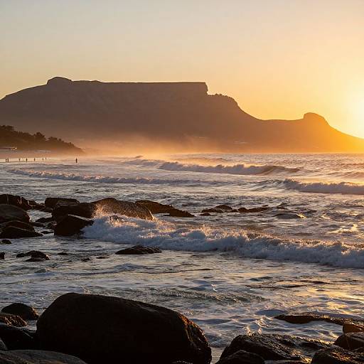 Photograph of a sunset over a rocky ocean shoreline with waves crashing, silhouetted cliffs, and a golden sky reflecting on water.
