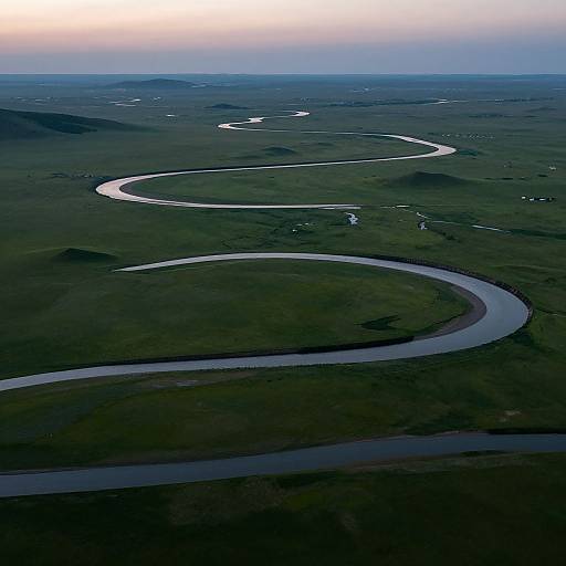 Aerial photograph of a winding river snaking through a vast, dark green landscape under a pale blue and pink sky.