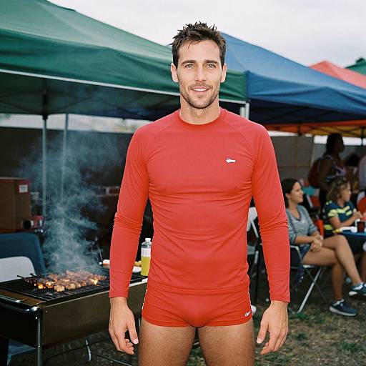 Photograph of a smiling, fit, dark-haired man in a red long-sleeve rash guard and matching red briefs, standing in front of