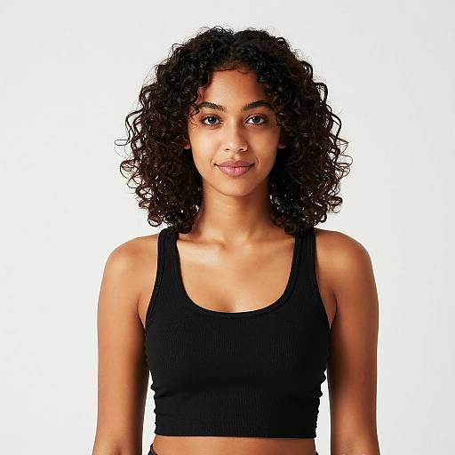Photograph of a young woman with medium brown skin, curly black hair, and brown eyes, wearing a black ribbed tank top, smiling against a