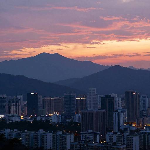 Photograph of a cityscape at dusk, with tall buildings in the foreground, silhouetted against a pink and orange sunset sky, and dark