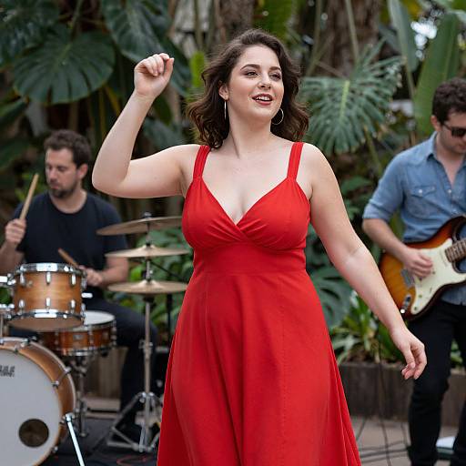 Photograph of a smiling, curvy woman with fair skin and dark hair in a red, V-neck dress, dancing with a band in a lush
