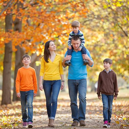 Photograph of a family with two parents and three children walking in a forest with autumn leaves. Father carries youngest son, children in orange, yellow,