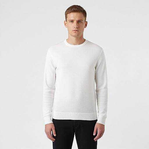 Photograph of a young, fair-skinned man with short brown hair, wearing a plain white long-sleeve sweater and black pants, standing against