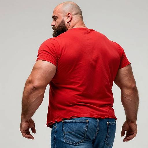 Photograph of a muscular, bald, bearded man in a red, slightly torn t-shirt and blue jeans, viewed from the back.