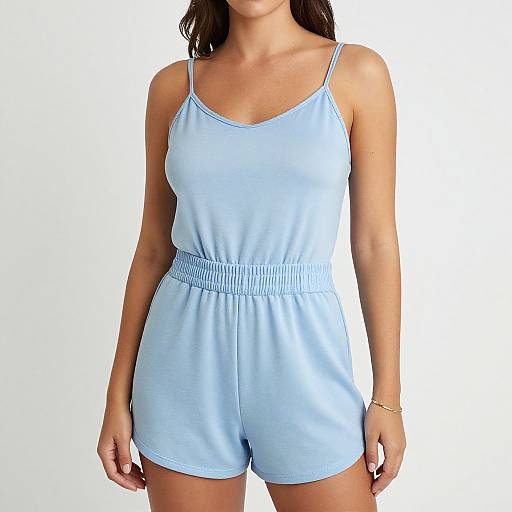 Photograph of a woman in light blue, spaghetti-strap romper with elastic waistband, standing against a plain white background, wearing a gold bracelet