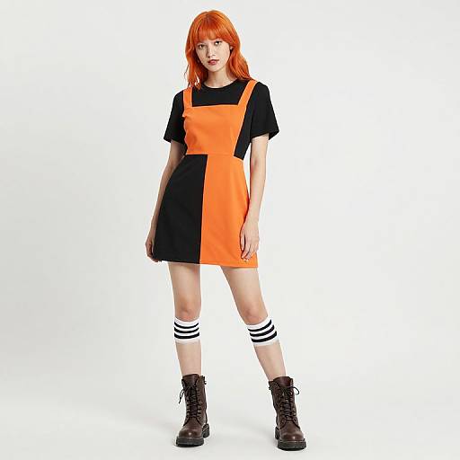 Photograph of a pale-skinned woman with red hair, wearing an orange and black dress, black t-shirt, striped knee-high socks, and brown