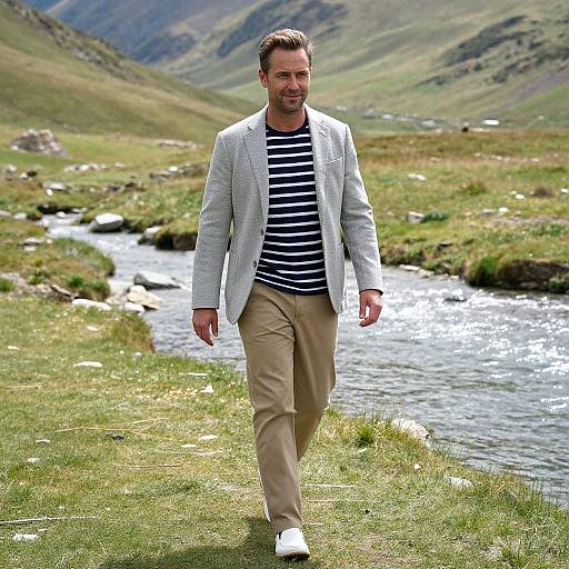 Photograph of a smiling man with short dark hair, wearing a light grey blazer, black and white striped shirt, beige pants, and white sneakers