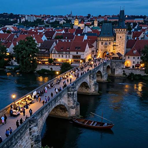 Photograph of Nuremberg's illuminated Stone Bridge at dusk, crowded with pedestrians, reflecting in the river, with historic buildings and a castle tower