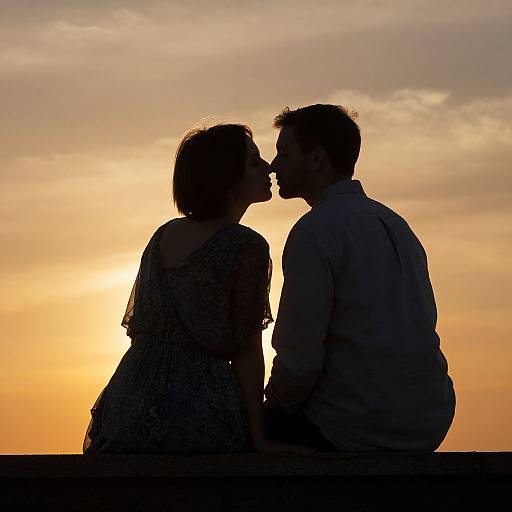 Silhouetted photograph of a couple kissing at sunset, with the golden sky and soft clouds in the background.