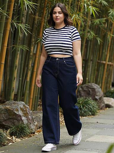 Photograph of a young woman with medium skin tone and dark hair, wearing a black-and-white striped shirt, high-waisted black pants, and