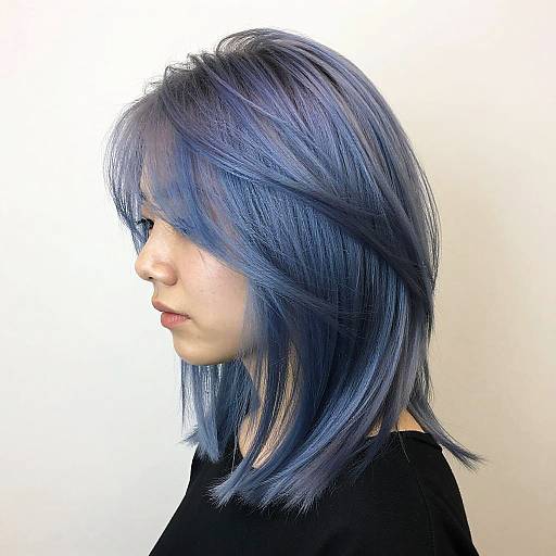 Photograph of a young woman with shoulder-length, blue and purple dyed hair in profile, wearing a black top, against a white background.