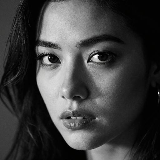 Black-and-white close-up photograph of a young woman with medium-length dark hair, striking eyes, and slightly parted lips, illuminated from the left.