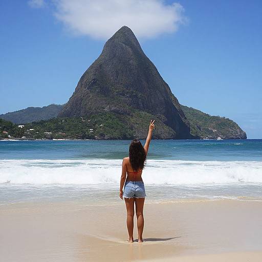 Photograph of a woman with long black hair, tan skin, and white bikini, standing on a beach, raising her right arm, facing a towering