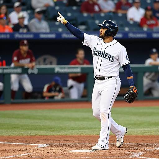 Photograph of a Seattle Mariners baseball player in white uniform, black helmet, pointing with gloved hand, walking on dirt field.