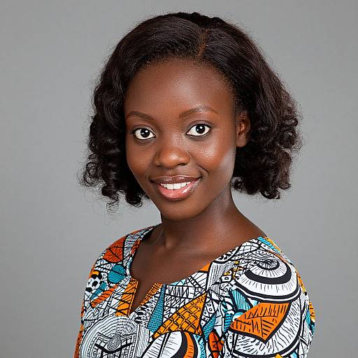 Photograph of a smiling African woman with dark skin and curly black hair, wearing a colorful, abstract-patterned top against a plain gray background.
