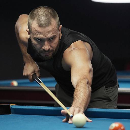 Photograph of a muscular, bald, middle-aged man in a black sleeveless shirt, intensely aiming to strike a pool ball with a cue stick on