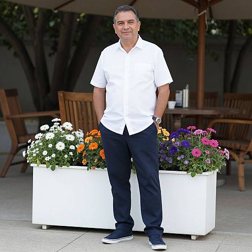 Photograph of a middle-aged man with short black hair, wearing a white shirt, black pants, and black sneakers, standing in front of a white