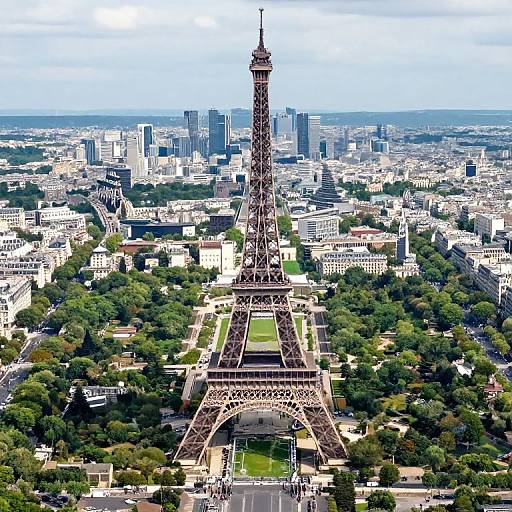 Aerial photograph of the Eiffel Tower in Paris, surrounded by green parks and city buildings, with a clear blue sky overhead.