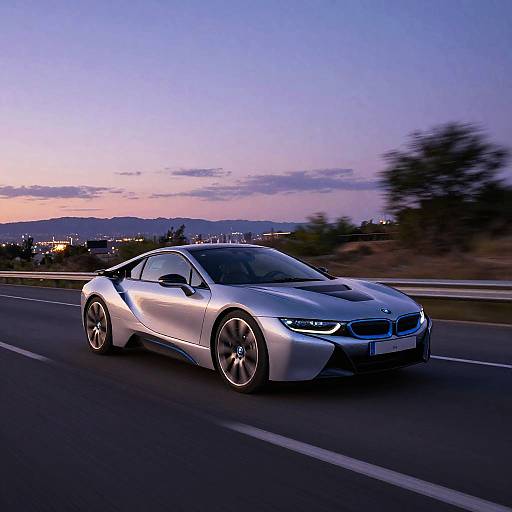 Photograph of a sleek, silver BMW i8 sports car speeding on a highway at dusk, with a purple and pink sunset sky in the background.