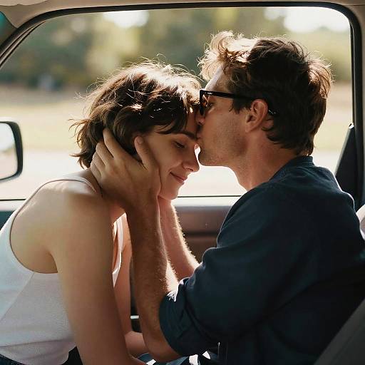 Photograph of a couple inside a car, man with dark sunglasses gently touching woman's head, both leaning in for a kiss, sunlit background.