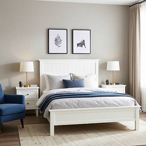 Modern bedroom photograph: White bed with blue blanket, white pillows, two black-framed art pieces, blue armchair, white nightstands, white lamps