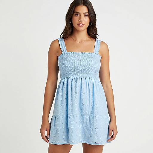 Photograph of a young woman with dark brown hair, wearing a light blue, sleeveless, lace-embroidered, sundress, standing against