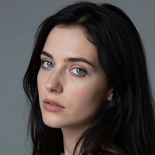 Photograph of a young woman with pale skin, blue eyes, and long black hair, gazing slightly to the left against a gray background.